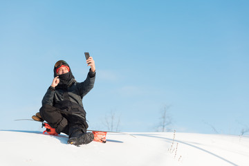 Fototapeta na wymiar happy man taking a selfie while resting after snowboarding. full length photo. copy space. blue sky on the background of the photo. leisure time