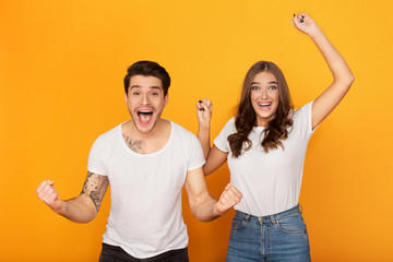 Couple clenching fists like winners over yellow background