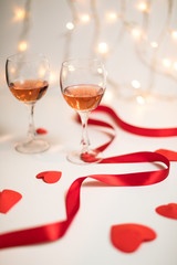 Valentine's day preparation with glasses of rose wine, red ribbon, hearts and fairy lights in the backgroung