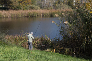 Man catches fish by the lake on a sunny autumn day.