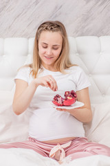 Obraz na płótnie Canvas Smiling pregnant woman eating red pomegranate, to increase hemoglobin
