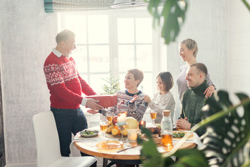 positive family exchanging gifts at new year.old man is diving a box to his daughter