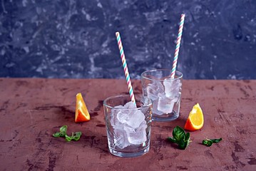 Glass glass with ice cubes and a straw prepared for a refreshing orange cocktail.