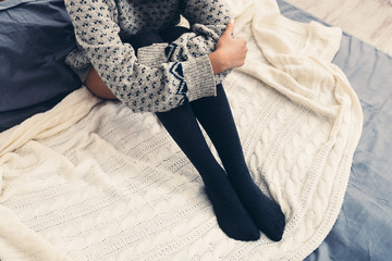 Woman sitting in bed, wearing warm sweater and stockings,