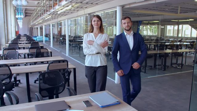 employees stop in front of the camera looking with successful smile two young white-collar workers walking around the office