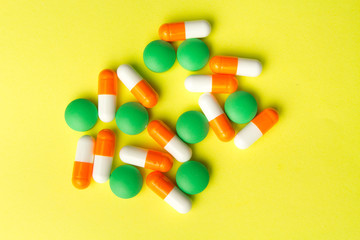 Medicine green pills and orange capsules on yellow background with copy space. Drug prescription for treatment medicine. Medical background, template