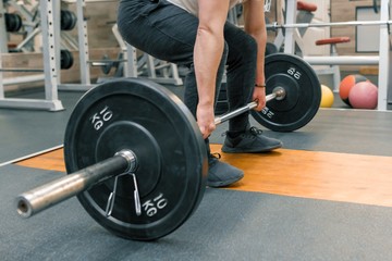 Fototapeta na wymiar Closeup of arms and legs of man exercising with barbell at sport gym. Athlete, bodybuilding, training, weightlifting, workout exercises concept