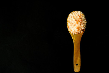 Fototapeta na wymiar Wooden kitchen spoon with Himalayan salt, black background, selective focus, free copy space
