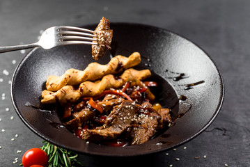 A meat dish with bread sticks and spices on black background