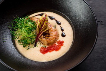 Tasty cream soup with red caviar and shrimp on black background