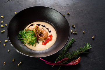 Tasty cream soup with red caviar and shrimp on black background