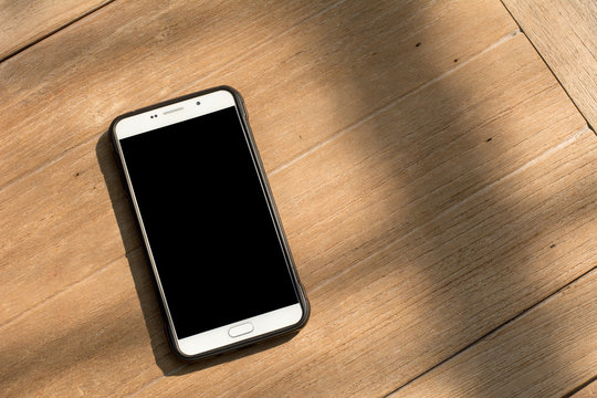 Mobile phone with blank black screen on wooden table background