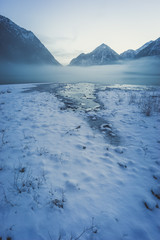 Winterliches Alpenpanorama mit Spiegelung und Nebel am See im Winter, Heiterwanger See, Tirol, Österreich