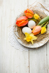 Ostern - Osternest auf silberen Teller mit orangefarbene Tulpen mit Narzissen auf Holz