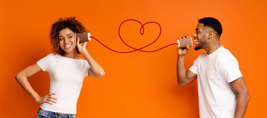 Young black couple with can phone on orange background