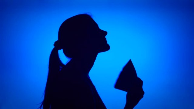 Silhouette of young successful woman count bundle of money on blue background. Female's face in profile with pile of bills. Black contur shadow of teenager's half-face. Concept of wealth and success