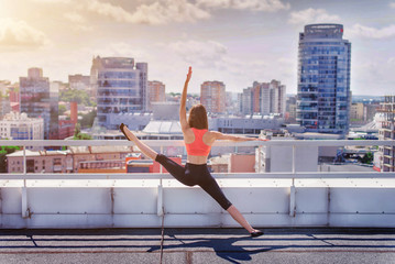Sports girl doing yoga and pilates on the roof of a skyscraper