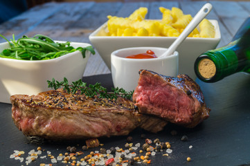 Grilled steak with french fries and served on black stone on wooden table