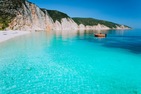 Small red boat on clear blue sea water near to amazing beach on mediterranean island. Summer beach vacation relaxation concept