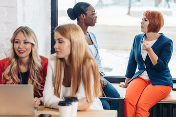 Obraz premium Group of young modern women in bright colourful casual wear discussing topics while sitting in the coffee shop