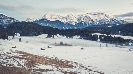 Fototapeta na wymiar Holzhütten auf schneebedeckter Alm mit traumhafter Bergkulisse