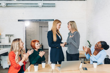 Happy blonde female boss promoting employee to a new position, hand shaking with female co-worker...
