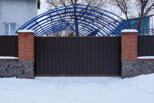 brown metal gates and a brick fence outside in white snow drifts