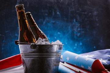 two bottles of beer in an ice bucket with the American flag lying nearby and rockets for fireworks....