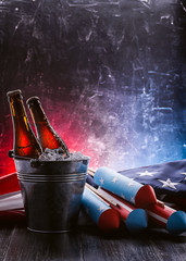 two bottles of beer in an ice bucket with the American flag lying nearby and rockets for fireworks....