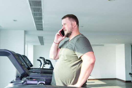Sweating chubby man walking on running track, warming up on gym treadmill