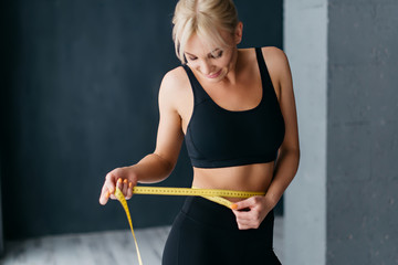 Athletic slim woman measuring her waist by measure tape