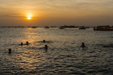 Beautiful view of the silhouettes of the children playing in the sea making splashes of the water lit by sunset backlight.Silhouette of a children. Stone Town, Zanzibar, Tanzania.