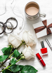 Women's table beautiful background. Bouquet of roses, gift box, leather bracelets, lipstick, headphones, coffee on a light background, top view. Valentine's day background, beauty concept