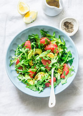 Avocado, grapefruit, rocket salad with mustard olive oil salad dressing on light background, top view. Vegetarian diet food concept