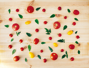 Naklejka na ściany i meble Food composition with red and yellow tomatoes and green leaves on light wooden background