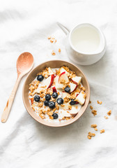 Peanut butter granola with milk, apples and blueberries - healthy energy breakfast or snack on a light background, top view. Copy space