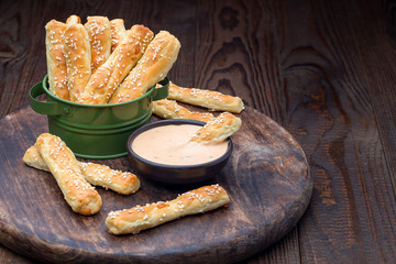 Homemade savory bread sticks with cheese and sesame in a basket, served with sauce on wooden board, horizontal, copy space