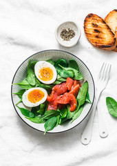 Delicious brunch - spinach, smoked salmon, soft boiled egg on a light background, top view. Healthy eating diet concept