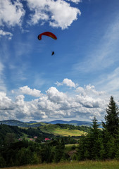 Paraglider flying over mountains during summer day