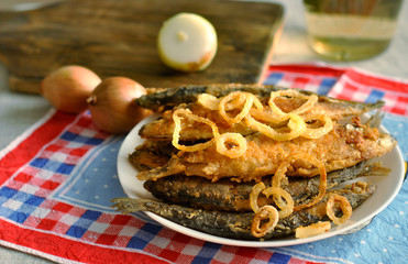 Fried fish and fried onions in a white plate on a beautiful napkin. Still life