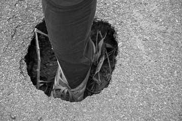 Monochrome background with a female leg in a hole in the asphalt