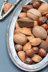 Different kinds of nuts in the shell: hazelnut, walnut, almond and brazil nuts on the plate with nut cracker on background, vertical