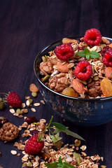 Granola made of oatmeal flakes, nuts and seeds decorated with big raspberries against the dark background