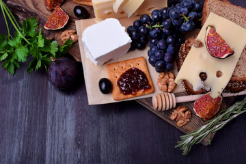 Assortment of appetizers: different sorts of cheese, crackers, grapes, nuts, olive marmalade, figs and olives against the dark background