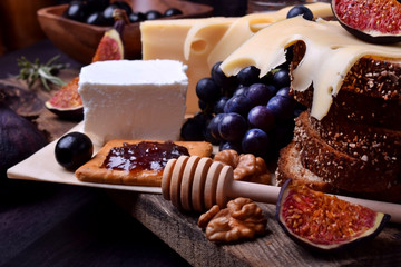 Assortment of appetizers: different sorts of cheese, crackers, grapes, nuts, olive marmalade, figs and olives against the dark background