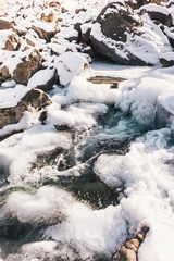 Winter mountain river under ice. Water froze and turned into icicles.