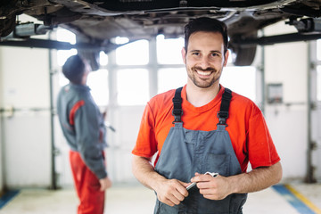 Two mechanics in uniform are working in auto service with lifted vehicle