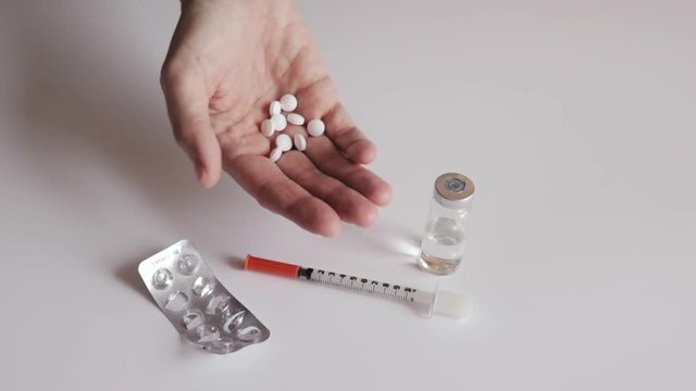 A woman showing white tablets in hand, empty blister, siringe and vial on white table background