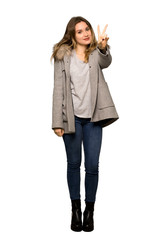 A full-length shot of a Teenager girl with coat smiling and showing victory sign on isolated white background
