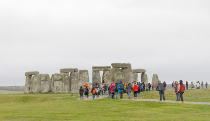 Tourists watching the stone monument Stonehenge a cloudy day,  built in the late Neolithic period,...